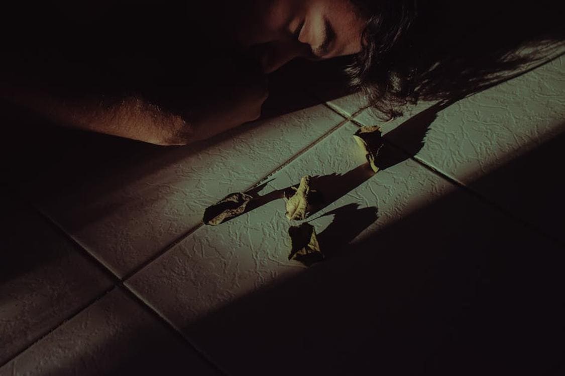 How Epoxy Flooring Stands Up to Tough Garage Conditions a dramatic shot of a person lying on the floor surrounded by dried leaves  emphasizing shadows and mood - How Epoxy Flooring Stands Up to Tough Garage Conditions