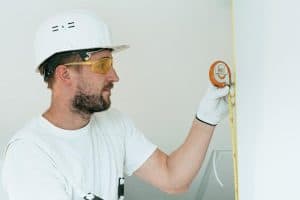 construction worker with hard hat and goggles measuring a wall with a tape measure 300x200 - construction worker with hard hat and goggles measuring a wall with a tape measure..jpg